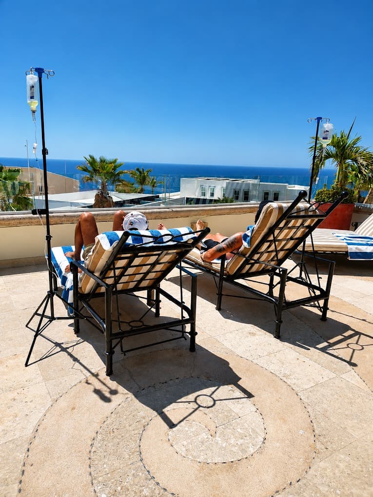 Two guests receiving IV hydration on rooftop lounge chairs with an ocean view